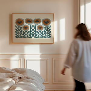 May include: A framed floral art print featuring stylized flowers in shades of teal, orange, and cream. The artwork is displayed on a light-colored wall in a bedroom setting. The frame is a light wood color.
