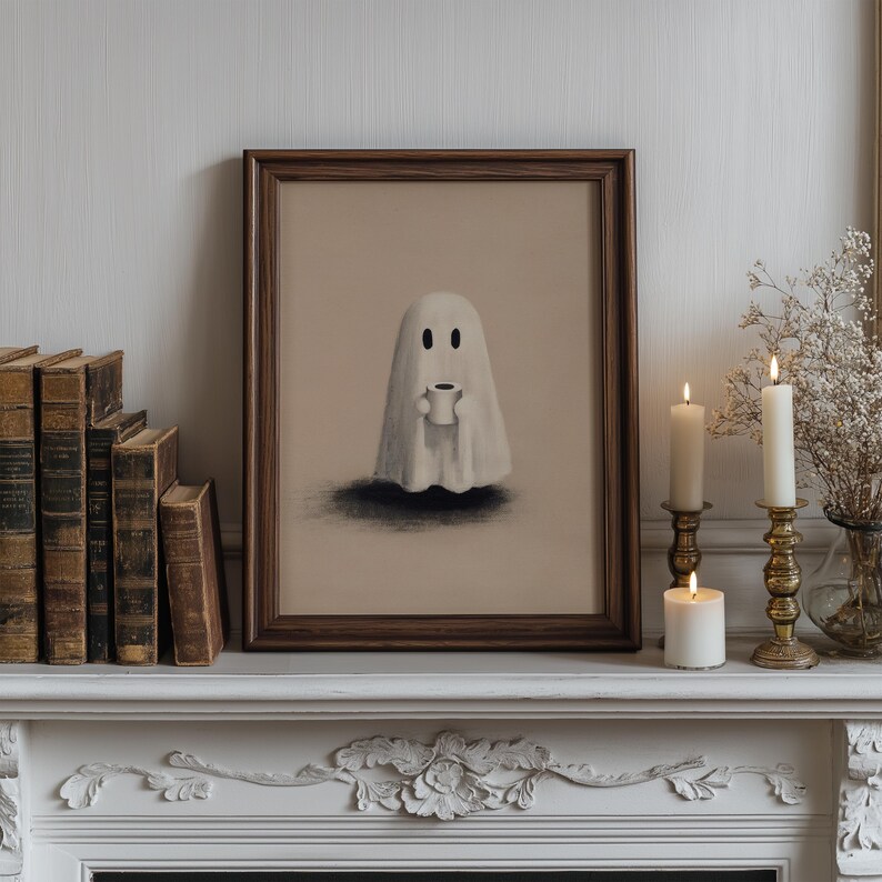 May include: A framed print featuring a whimsical ghost holding a coffee cup. The artwork is set against a neutral background and framed in dark wood. The scene is complemented by lit candles in ornate holders, creating a cozy, Halloween-themed aesthetic.