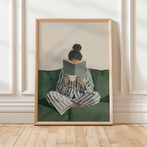 May include: A framed art print depicts a person in striped pajamas reading a book while seated on a green sofa. The person holds a cup of coffee. The artwork has a neutral color palette with a wooden frame.