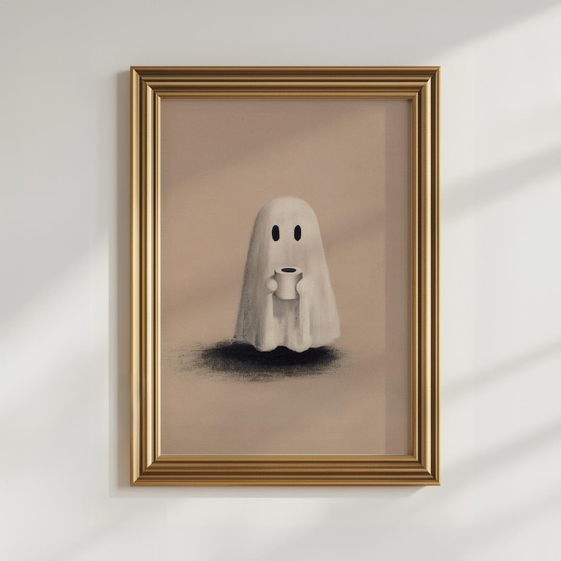 May include: Framed art print featuring a whimsical ghost holding a coffee cup. The ghost is depicted in a simple, cartoonish style with a white sheet and black eyes. The artwork is set against a neutral background, framed in gold.