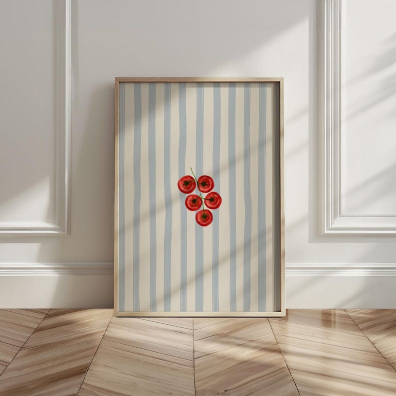 May include: A framed art print featuring a cluster of five red tomatoes on a green stem. The background has vertical stripes of light blue and beige. The frame is a light brown color.
