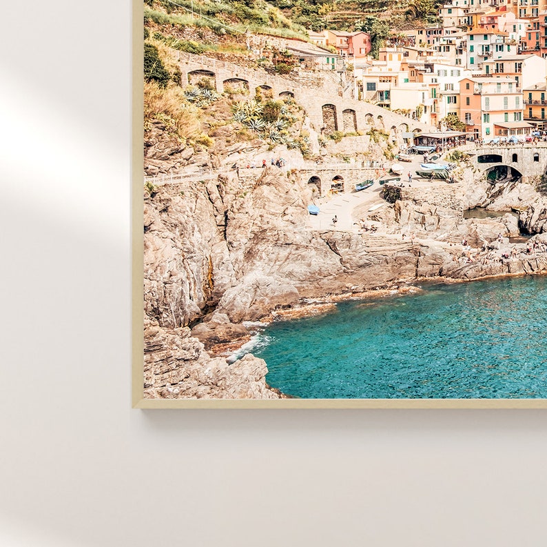 May include: A colorful, hillside village with buildings cascading down to a rocky coastline. The turquoise water of the Mediterranean Sea laps at the shore.