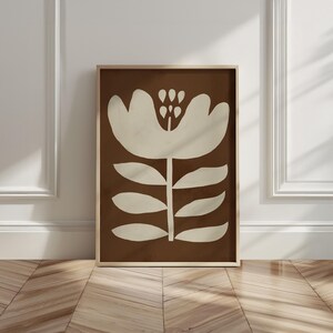 Pu&ograve; includere: Stampa artistica incorniciata con un design floreale stilizzato. L'opera presenta un grande fiore bianco sporco su uno sfondo marrone. La stampa &egrave; racchiusa in una cornice di legno marrone chiaro, aggiungendo calore al design.
