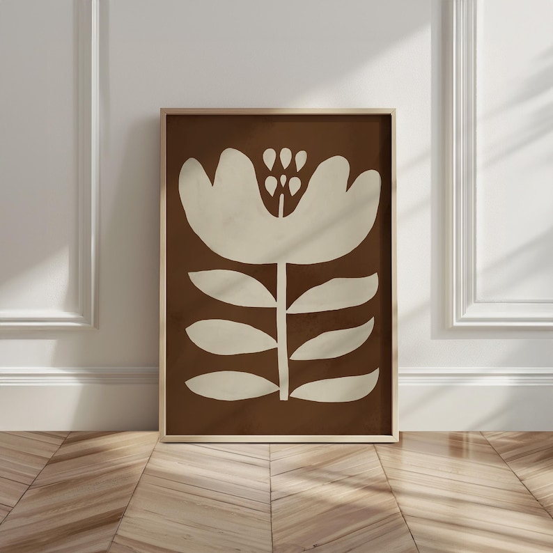 Pu&ograve; includere: Stampa artistica incorniciata con un design floreale stilizzato. L'opera presenta un grande fiore bianco sporco su uno sfondo marrone. La stampa &egrave; racchiusa in una cornice di legno marrone chiaro, aggiungendo calore al design.
