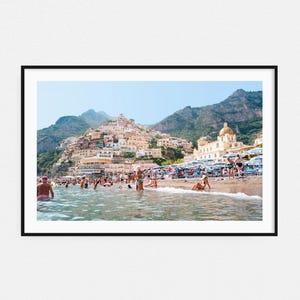 May include: A colorful cityscape with a beach in the foreground. The buildings are built into a hillside with a church at the top. People are swimming and sunbathing on the beach.