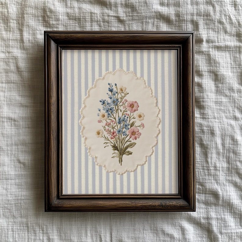 K&ouml;nnte beinhalten: Gerahmte Blumenstickerei mit einem Bouquet aus rosa, blauen und gelben Blumen. Die Stickerei befindet sich vor einem gestreiften Hintergrund aus hellblau und wei&szlig;, in einem dunkelbraunen Holzrahmen.