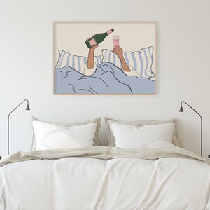 May include: A digital illustration of a person in bed with a glass of pink champagne and a bottle of champagne. The person is under a blue blanket with white stripes. The background is a light beige colour.