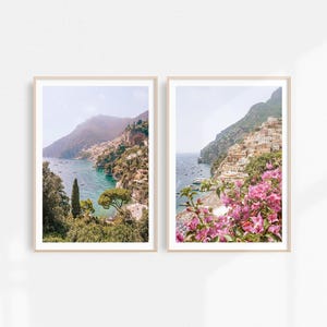May include: Two framed photographs of a coastal town in Italy. The left photo shows a view of the town from the water, with lush green trees and mountains in the background. The right photo shows a closer view of the town, with pink flowers in the foreground.