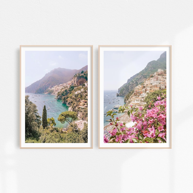 May include: Two framed photographs of a coastal town in Italy. The left photo shows a view of the town from the water, with lush green trees and mountains in the background. The right photo shows a closer view of the town, with pink flowers in the foreground.