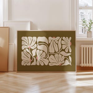 May include: A framed floral art print featuring a botanical design. The artwork showcases stylized cream-colored flowers with pink centers against an olive green background. The print is displayed in a natural wood frame.