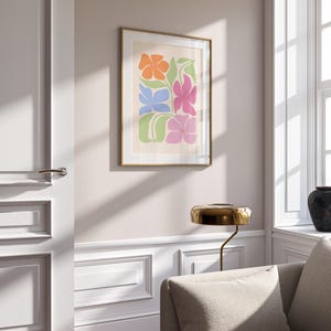 K&ouml;nnte beinhalten: Ein gerahmter Kunstdruck mit einem farbenfrohen Blumendesign. Das Kunstwerk zeigt stilisierte Blumen in Orange, Blau, Pink und Gr&uuml;n auf cremefarbenem Hintergrund. Der Druck ist in einem goldenen Rahmen eingefasst und verleiht der Wanddekoration einen Hauch von Eleganz.