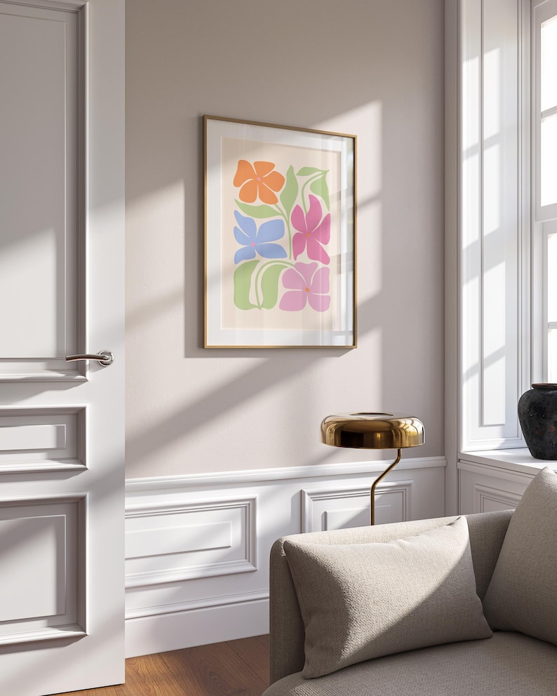 K&ouml;nnte beinhalten: Ein gerahmter Kunstdruck mit einem farbenfrohen Blumendesign. Das Kunstwerk zeigt stilisierte Blumen in Orange, Blau, Pink und Gr&uuml;n auf cremefarbenem Hintergrund. Der Druck ist in einem goldenen Rahmen eingefasst und verleiht der Wanddekoration einen Hauch von Eleganz.