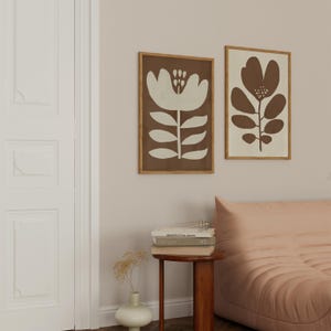 Pu&ograve; includere: Due stampe artistiche floreali incorniciate. Una presenta un fiore bianco su sfondo marrone, l'altra un design floreale marrone su crema. Entrambe sono in cornici di legno, per un tocco naturale.