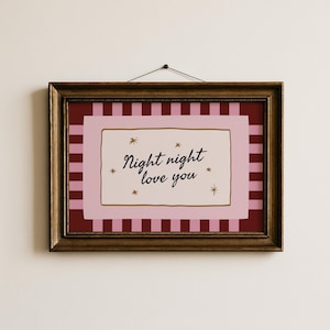May include: A framed art print with the words "Night night love you" in black script. The artwork features a pink and red striped background, a pink border, and gold star accents. The frame is a dark, ornate gold color.