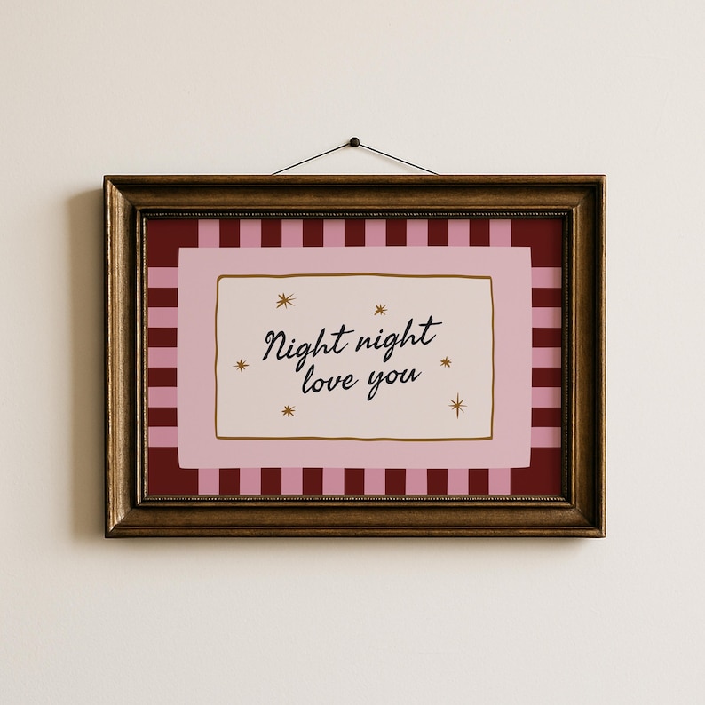 May include: A framed art print with the words "Night night love you" in black script. The artwork features a pink and red striped background, a pink border, and gold star accents. The frame is a dark, ornate gold color.