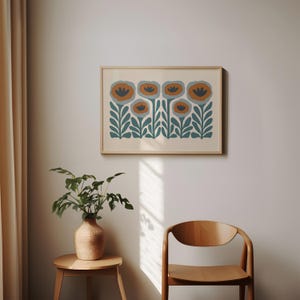 May include: A framed floral art print featuring stylized flowers in shades of orange, blue, and teal. The artwork is set against a cream-colored background and framed in a light wood. The print is displayed on a wall.