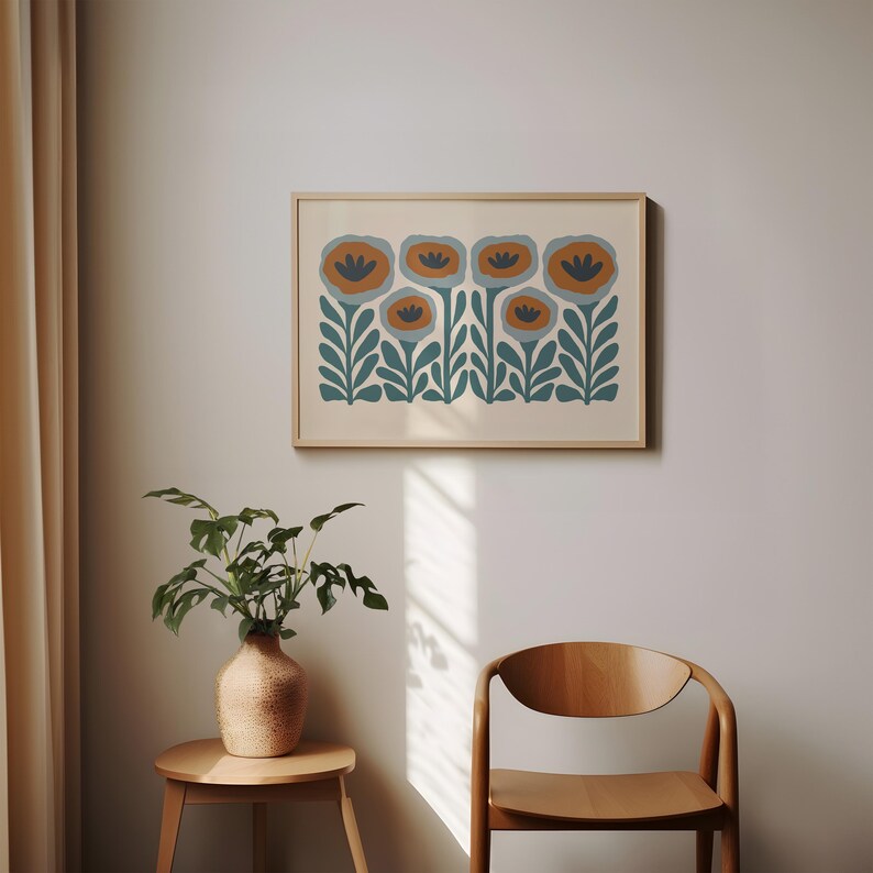 May include: A framed floral art print featuring stylized flowers in shades of orange, blue, and teal. The artwork is set against a cream-colored background and framed in a light wood. The print is displayed on a wall.