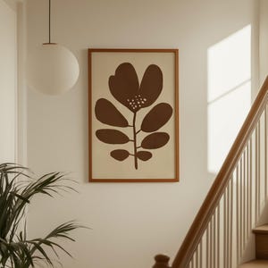 Pu&ograve; includere: Una stampa botanica incorniciata con un fiore marrone stilizzato con stelo e foglie. L'opera d'arte &egrave; ambientata su uno sfondo color crema e racchiusa in una cornice di legno. La stampa &egrave; esposta su una parete bianca.