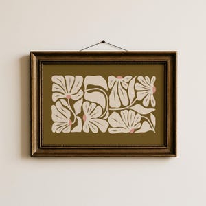 May include: A framed floral art print featuring a botanical design. The artwork showcases stylized cream-colored flowers with pink centers against an olive-green background. The frame is a dark brown color.