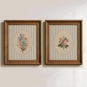 May include: Two framed floral prints. Each features a vintage-style oval with a floral bouquet on a striped background. One print has blue and pink flowers, the other has strawberries and white flowers. The frames are brown.