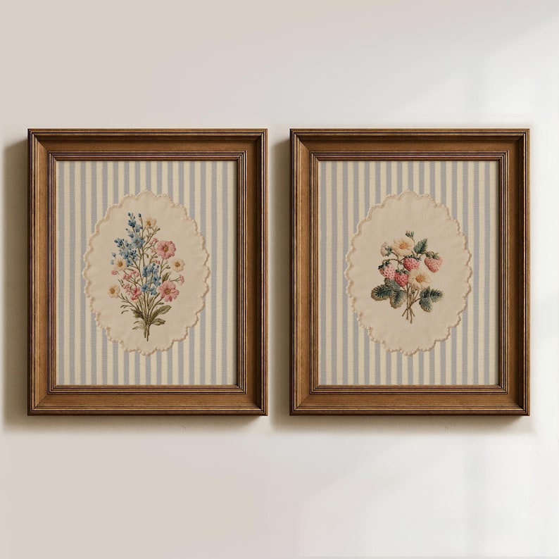May include: Two framed floral prints. Each features a vintage-style oval with a floral bouquet on a striped background. One print has blue and pink flowers, the other has strawberries and white flowers. The frames are brown.