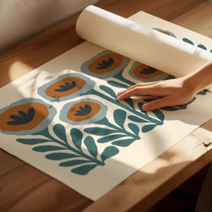 May include: A roll of floral wallpaper with a repeating pattern of stylized flowers in shades of orange, teal, and blue on an off-white background. The wallpaper is unrolled on a wooden surface.