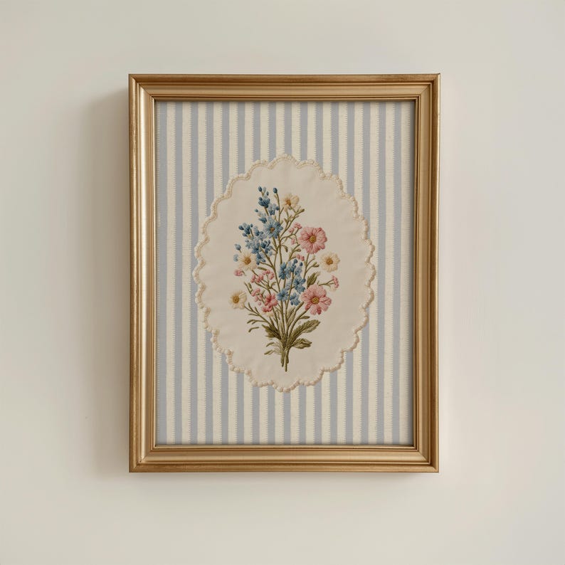 K&ouml;nnte beinhalten: Ein gerahmtes Blumenstickerei. Das Kunstwerk zeigt einen Strau&szlig; aus rosa, blauen und gelben Blumen auf einem ovalen, cremefarbenen Hintergrund mit einem gewellten Rand. Der Hintergrund ist ein hellblau-wei&szlig; gestreifter Stoff, der in einem goldfarbenen Rahmen eingefasst ist.