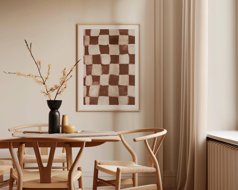 May include: A brown and white checkered abstract painting in a wooden frame hangs on a beige wall above a wooden dining table with two chairs.