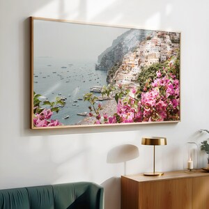 May include: A framed photograph of a coastal town in Italy with colorful buildings on a hillside overlooking the ocean. Pink flowers are in the foreground.