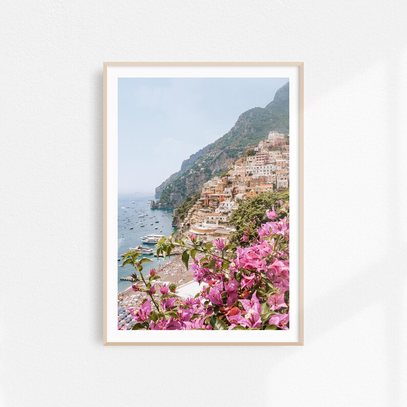 K&ouml;nnte beinhalten: Ein farbenfrohes Foto einer K&uuml;stenstadt in Italien. Die Stadt ist an einem steilen Abhang gebaut, mit Geb&auml;uden, die bis zum Wasser hinunterfallen. Das Meer ist tiefblau und es gibt Boote im Wasser. Der Vordergrund ist mit rosa Bougainvillea-Bl&uuml;ten gef&uuml;llt.