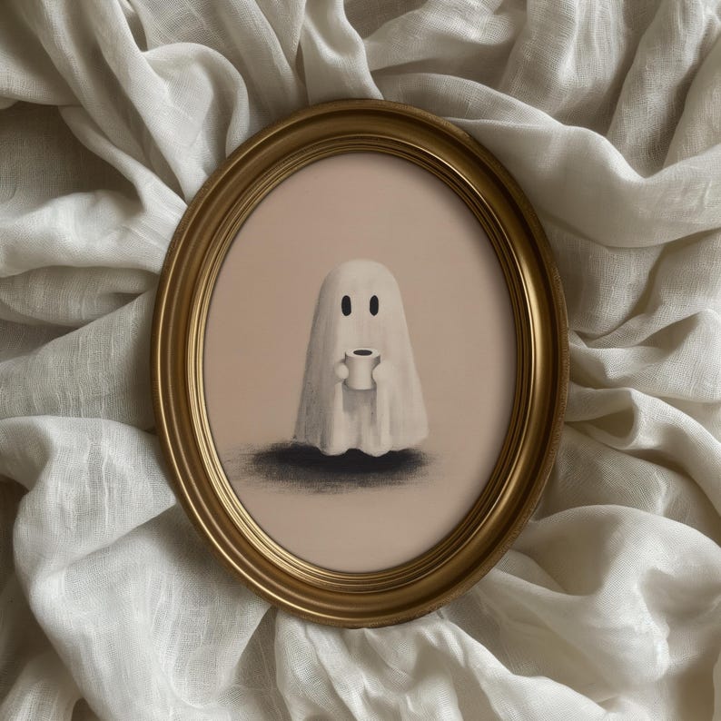 May include: An oval, gold-framed artwork featuring a whimsical ghost holding a small cup. The ghost is white with two black eyes, set against a pale pink background. The artwork has a soft, illustrative style, with a dark shadow beneath the ghost.