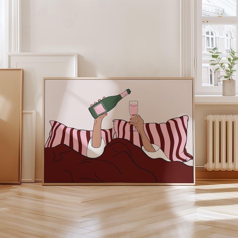K&ouml;nnte beinhalten: Gerahmter Kunstdruck, der eine Person im Bett zeigt, die Champagner einschenkt. Die Illustration zeigt eine gr&uuml;ne Champagnerflasche, ein rosa Glas und rosa-wei&szlig; gestreifte Kissen. Die Bettw&auml;sche ist dunkelrot.