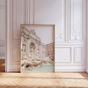 May include: A framed photograph of the Trevi Fountain in Rome, Italy. The fountain is made of white stone and has a large, cascading waterfall. The water is a light blue color. The fountain is surrounded by buildings and trees.