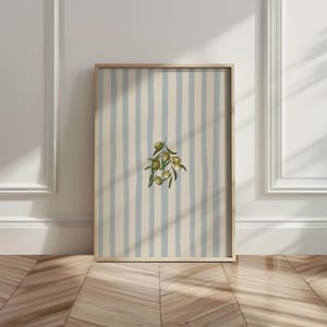 May include: Framed art print featuring a watercolor illustration of an olive branch with green olives. The background has vertical stripes in light blue and cream. The wooden frame adds a natural touch to the artwork, suitable for kitchen or dining room decor.
