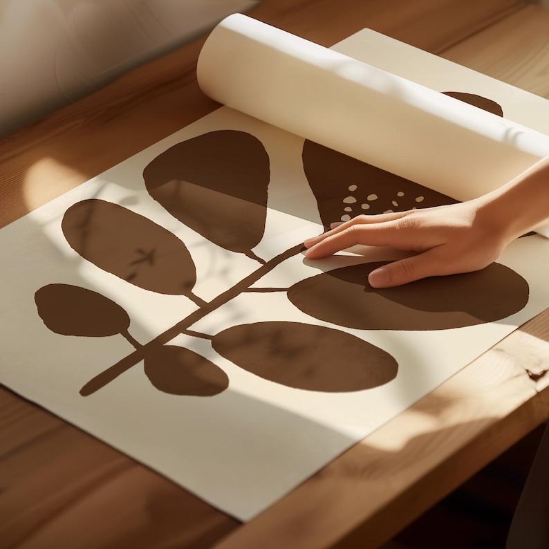 Pu&ograve; includere: Una stampa artistica con un design botanico marrone su sfondo bianco sporco. La stampa &egrave; parzialmente srotolata, rivelando un motivo di foglie e steli. L'immagine &egrave; su una superficie di legno.