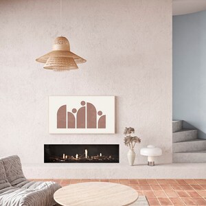 May include: A living room interior with a fireplace, a large, round, light-colored coffee table, a gray couch, a woven pendant light, and a framed print with a geometric design in shades of brown.