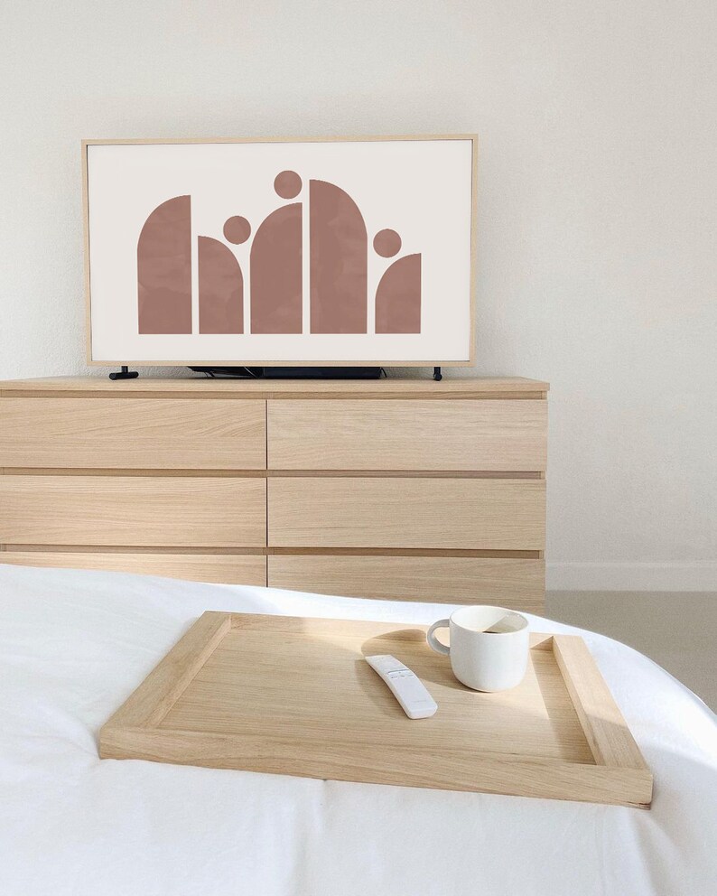 May include: A wooden tray with a white ceramic mug and a white remote control on a white bed. The tray is on top of a white bedspread.