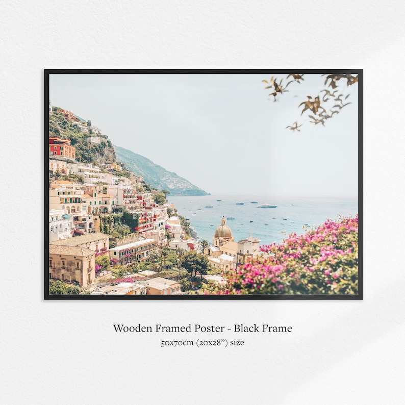 May include: A framed print of a coastal Italian town. The image features colorful buildings cascading down a hillside towards the sea. The print is in a black frame and measures 20x28 inches.