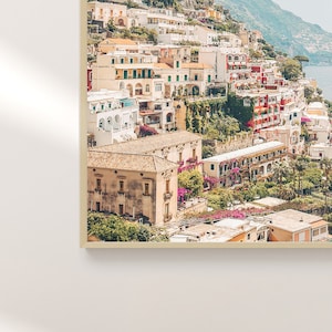 May include: A colorful aerial view of a hillside town with buildings clustered together. The buildings are a mix of yellow, white, red, and orange. There are lush green trees and plants growing on the hillside.