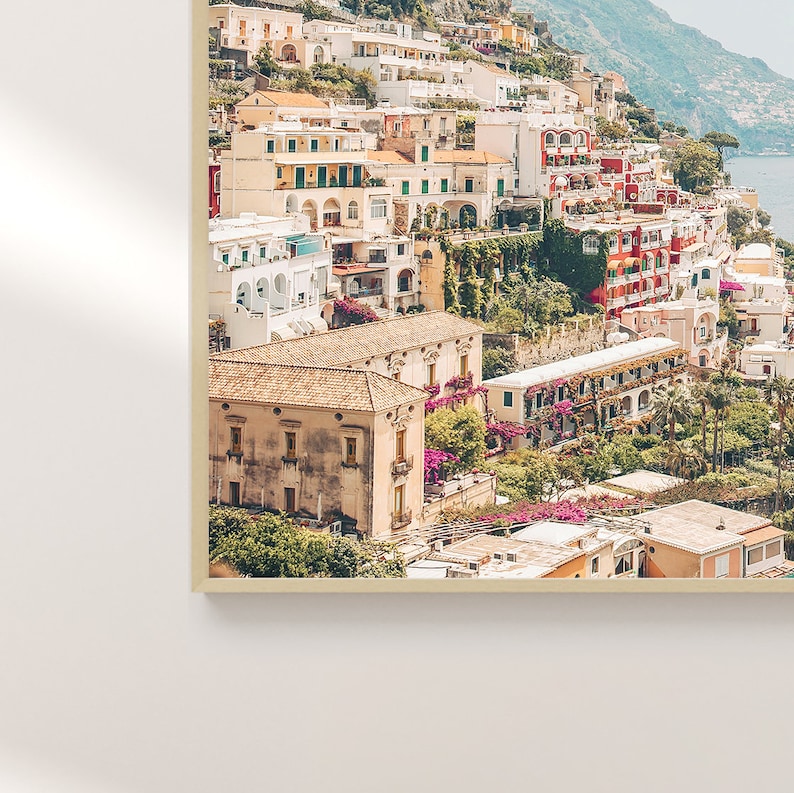 May include: A colorful aerial view of a hillside town with buildings clustered together. The buildings are a mix of yellow, white, red, and orange. There are lush green trees and plants growing on the hillside.