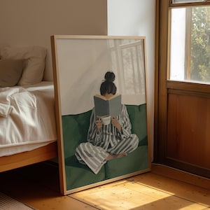 May include: A framed art print depicts a person in striped pajamas reading a book while seated on a green sofa. The person holds a cup of coffee. The artwork is set in a room with a window and a bed.