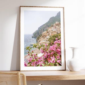 May include: A framed photograph of a colorful Italian village nestled on a cliffside overlooking a blue ocean. Pink bougainvillea flowers frame the bottom of the image.