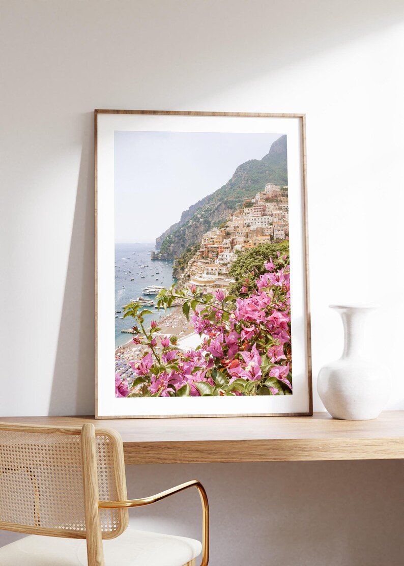 May include: A framed photograph of a colorful Italian village nestled on a cliffside overlooking a blue ocean. Pink bougainvillea flowers frame the bottom of the image.