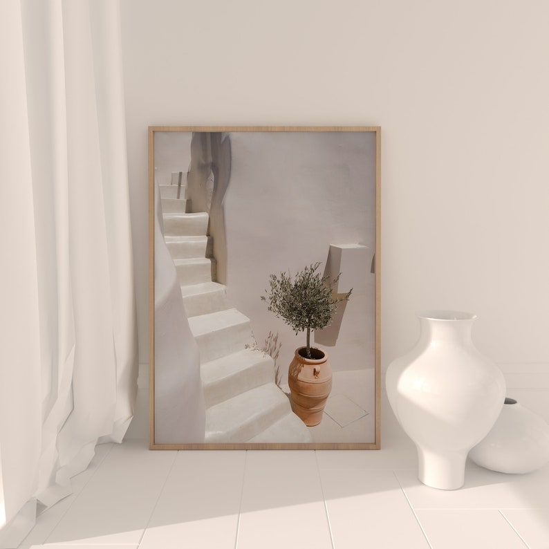 K&ouml;nnte beinhalten: Ein gerahmtes Foto einer wei&szlig;en Treppe mit einem kleinen Olivenbaum in einem Terrakotta-Topf. Die Treppe befindet sich in einem wei&szlig;en Geb&auml;ude mit einer wei&szlig;en Wand und einer wei&szlig;en T&uuml;r.