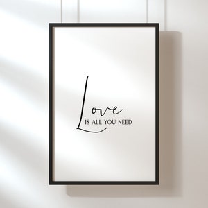Op de afbeelding: Een zwart ingelijst print met de tekst "Love is all you need" in een cursief lettertype.