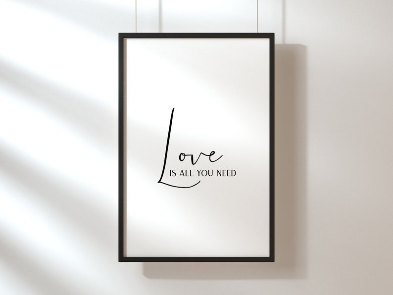 Op de afbeelding: Een zwart ingelijst print met de tekst "Love is all you need" in een cursief lettertype.