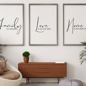 Op de afbeelding: Drie ingelijste prints met zwarte kalligrafie op een witte achtergrond. De prints luiden "Family is everything", "Love is all you need" en "Home is our happy place". De prints hangen aan een witte muur boven een houten dressoir.