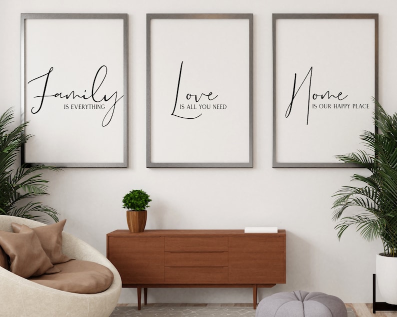 Op de afbeelding: Drie ingelijste prints met zwarte kalligrafie op een witte achtergrond. De prints luiden "Family is everything", "Love is all you need" en "Home is our happy place". De prints hangen aan een witte muur boven een houten dressoir.