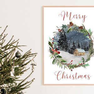 May include: A framed watercolor print with the words "Merry Christmas" in red script. The artwork depicts a snowy winter scene with a cabin nestled in a forest, surrounded by a wreath of greenery and berries. A Christmas tree is in the foreground.