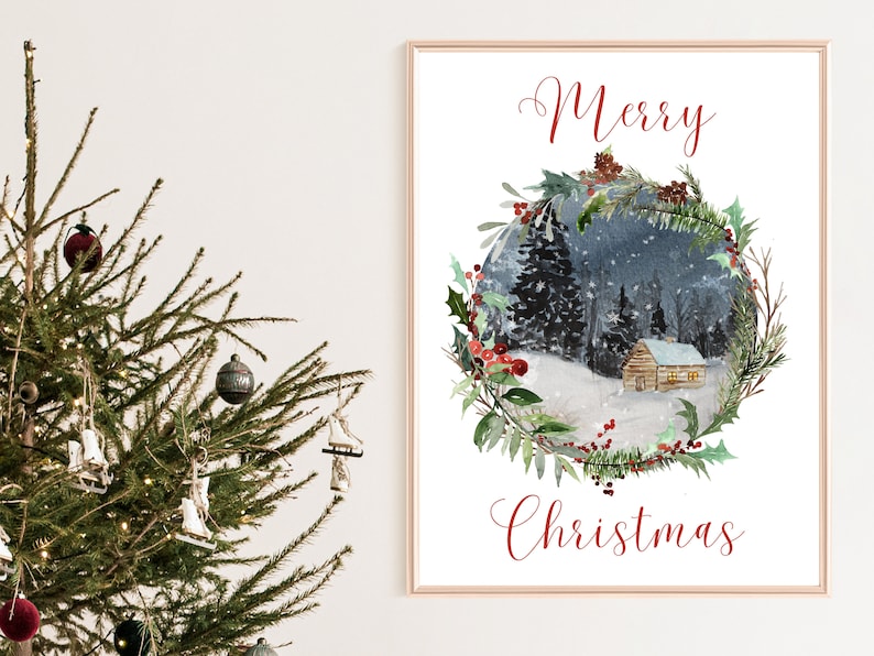 May include: A framed watercolor print with the words "Merry Christmas" in red script. The artwork depicts a snowy winter scene with a cabin nestled in a forest, surrounded by a wreath of greenery and berries. A Christmas tree is in the foreground.